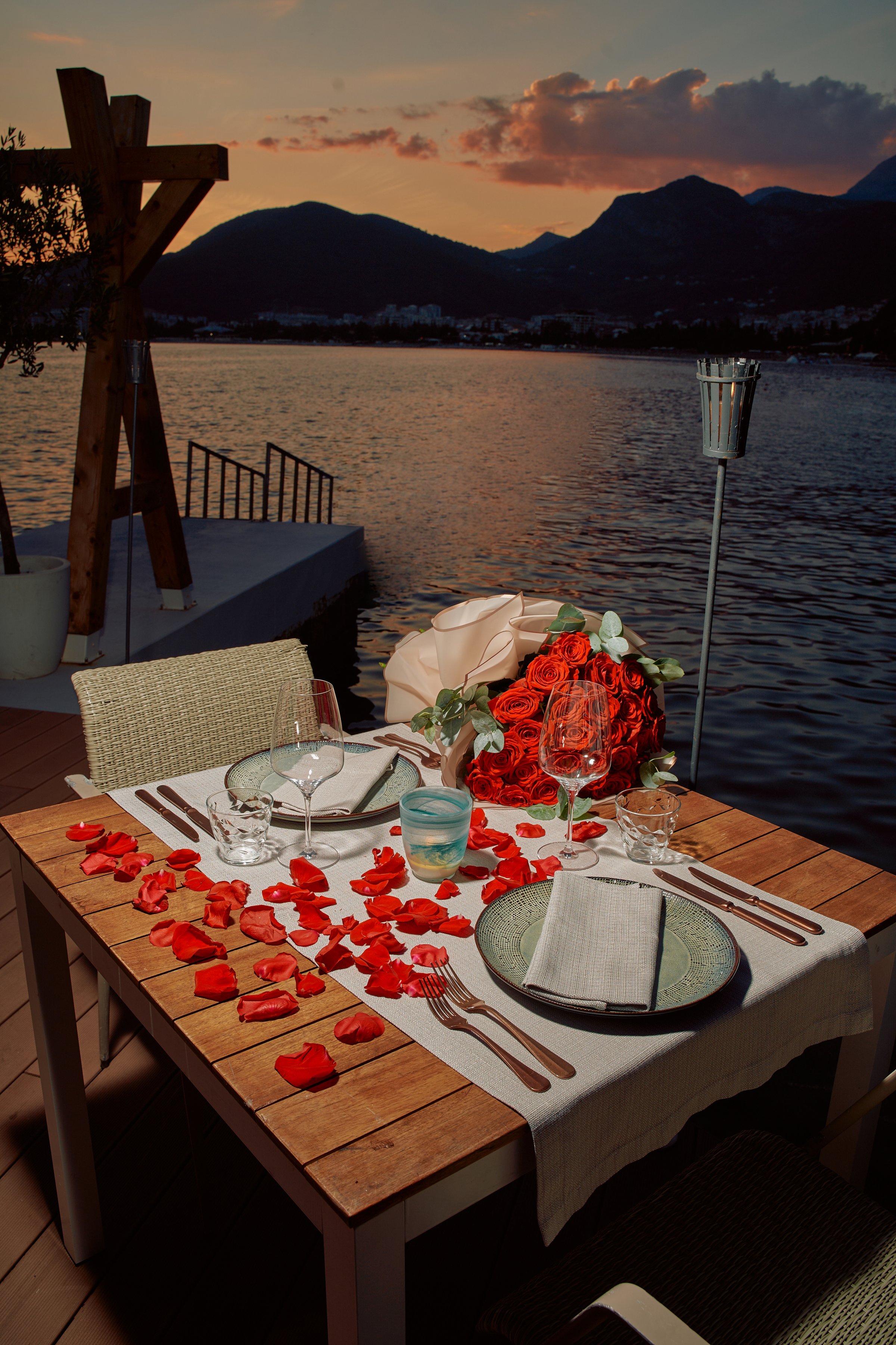 An Elegant Evening Dinner Setting by the Water with Roses and Romantic Details Under a Beautiful Sunset Sky