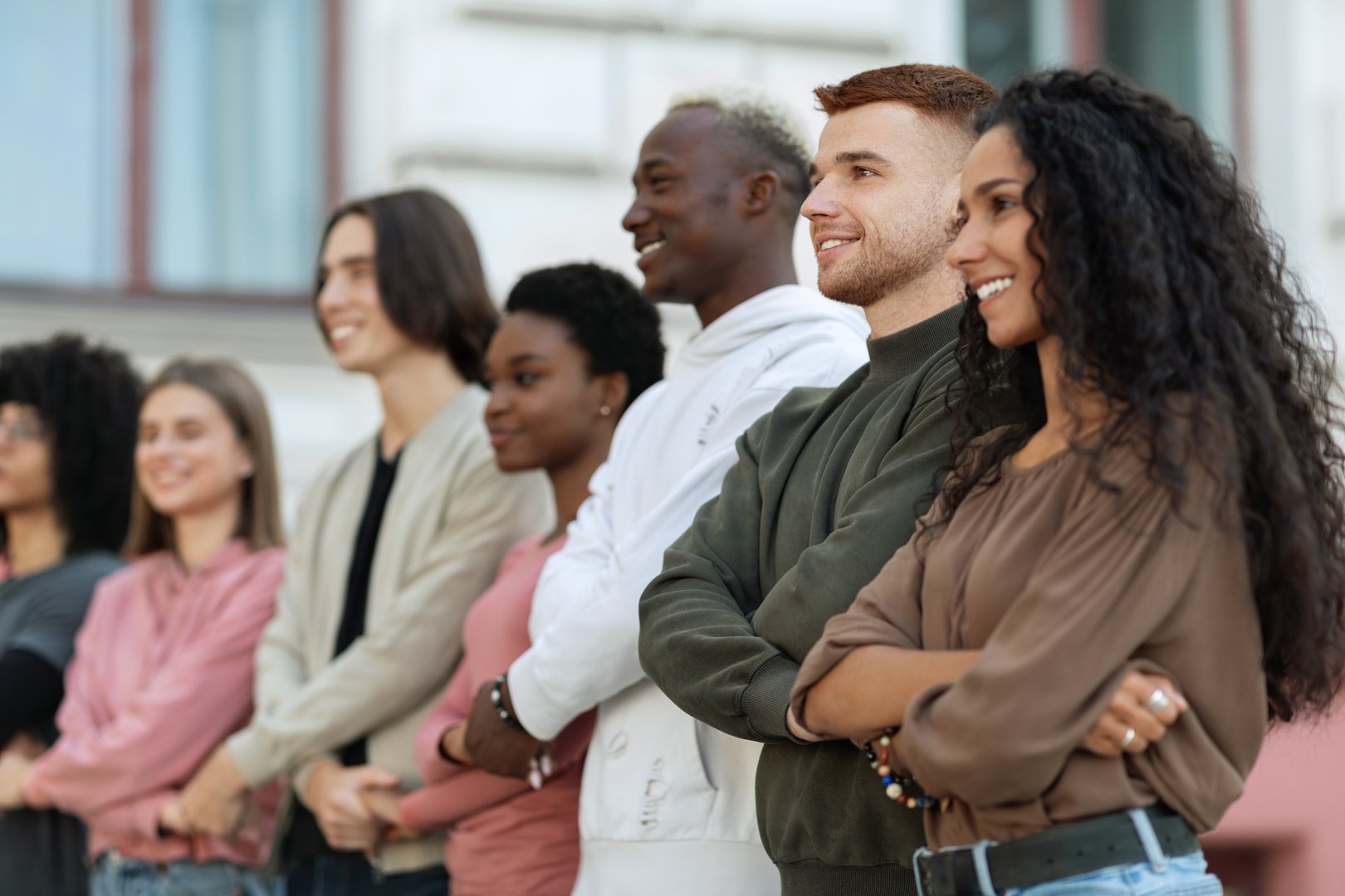 International group of cheerful students holding hands and chanting slogans while walking by street towards government building, multiracial activists having strike, feeling excited and invincible