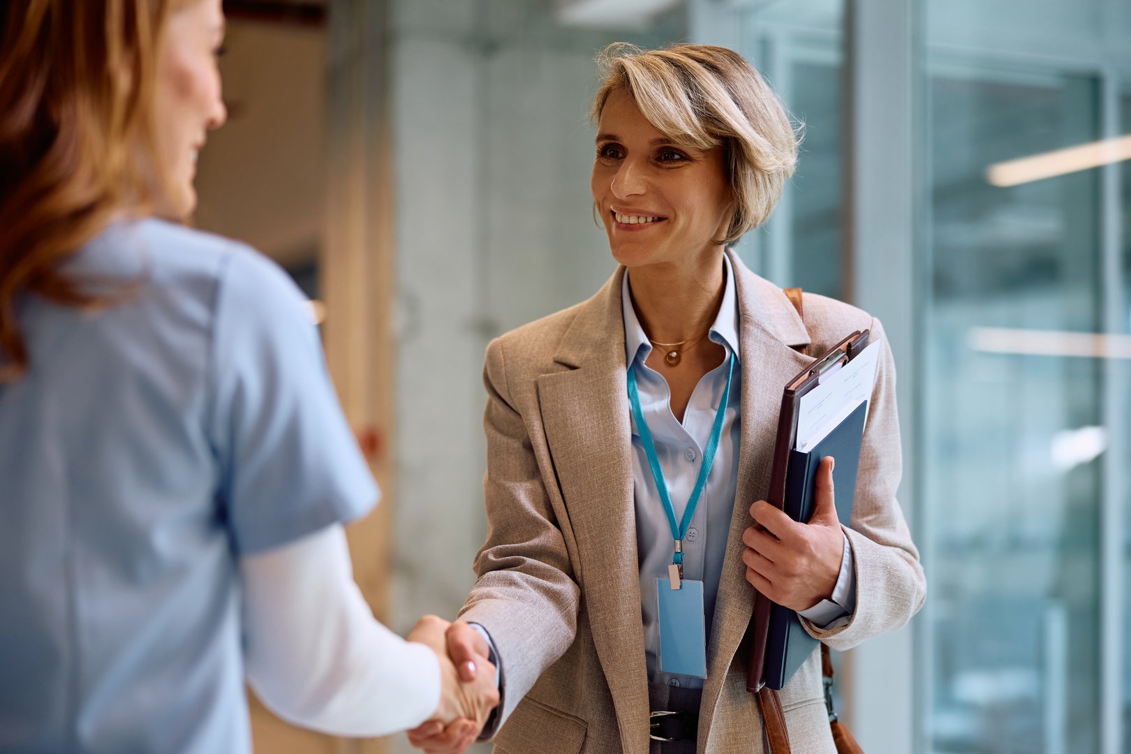 Happy businesswoman handshaking with female nurse at medical clinic.