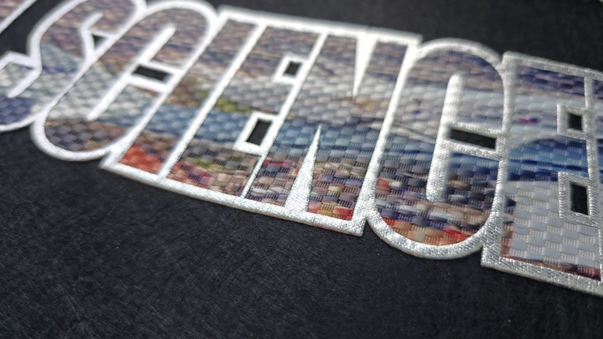 Close-up of the word SCIENCE in bold letters with a textured, multicolored pattern on a black background.