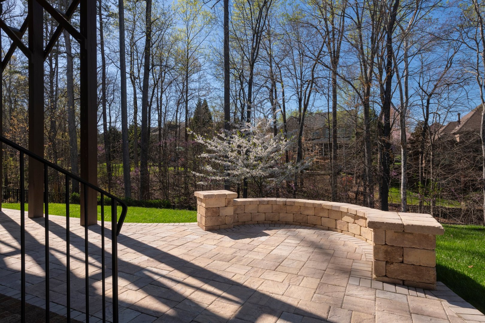 Picturesque backyard view in spring season with patio pavers and stone wall, blooming white cherry tree, and spring colored woods in the background.