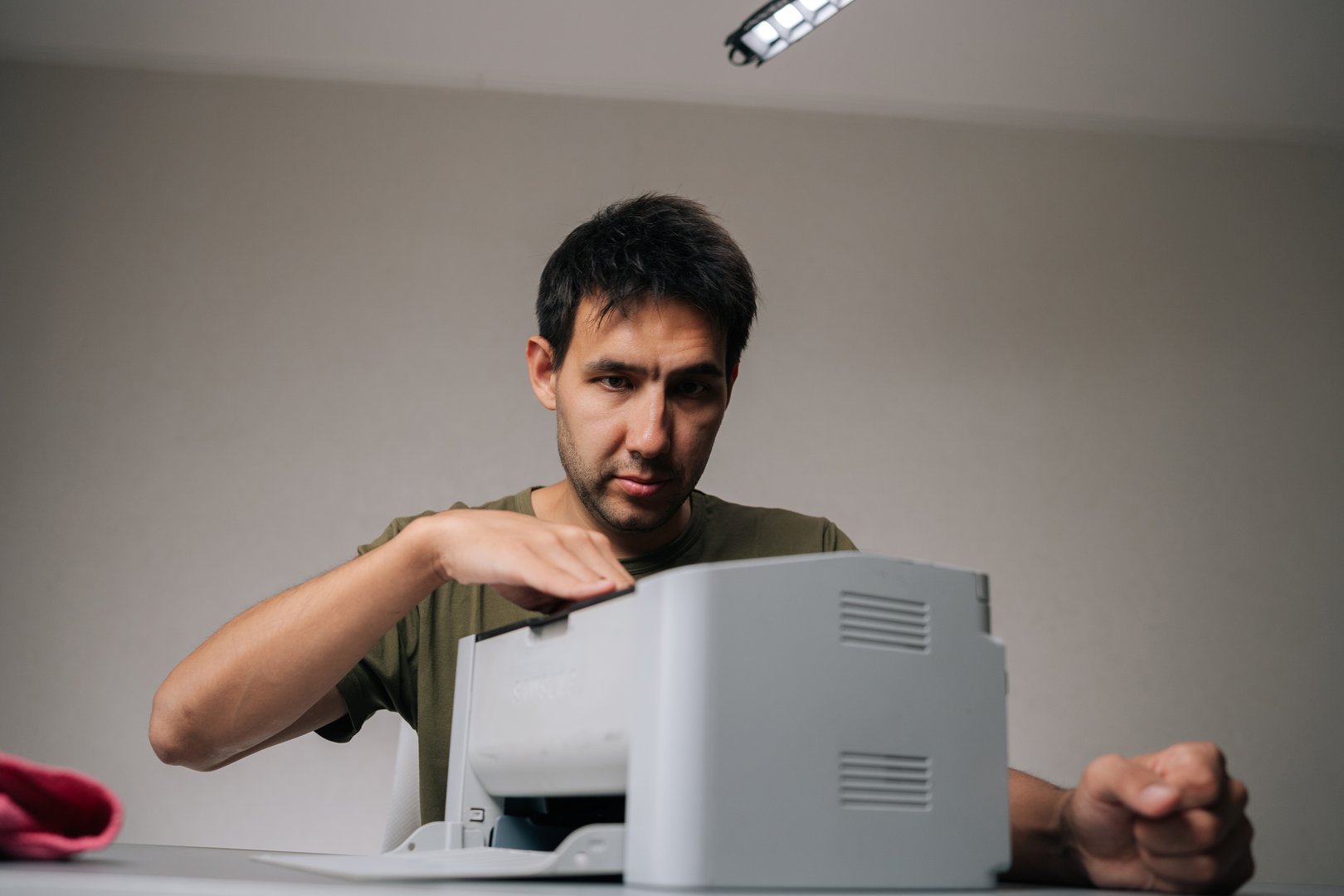 Portrait of young man wiping laser printer with microfiber cloth, performing regular maintenance