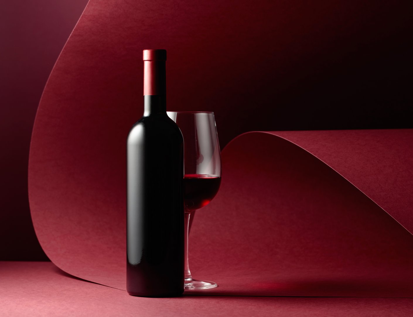 Bottle and glass of red wine on a red background. Copy space.