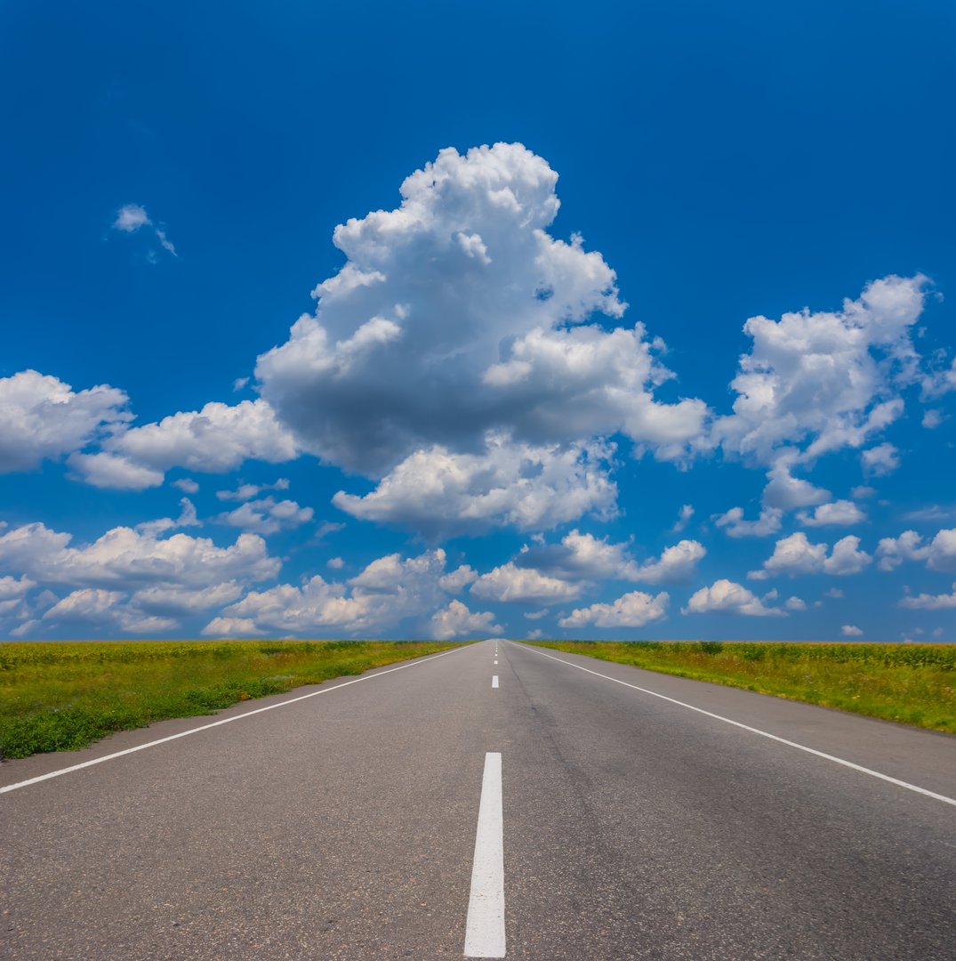 Long asphalt road among green fields