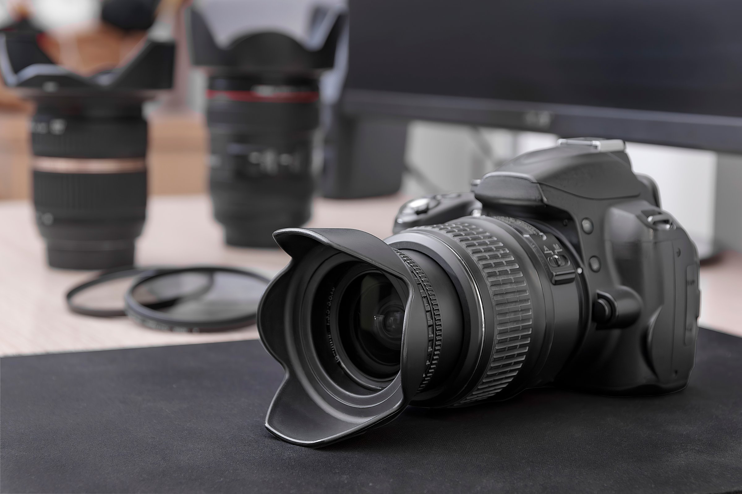 Digital SLR camera equipped with a lens and petal-shaped lens hood. In the background, two additional lenses and lens filters can be seen.