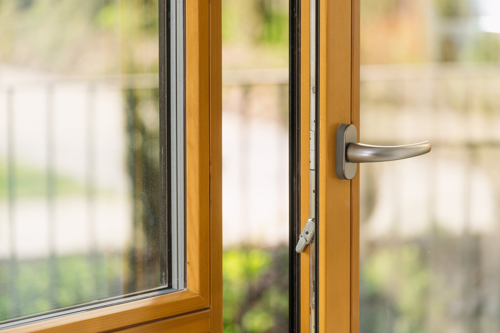 Close-up of a modern wooden window with a silver handle, open slightly. Balcony door in apartment. Blurred summer backyard against clear transparent glass, scenic view from room