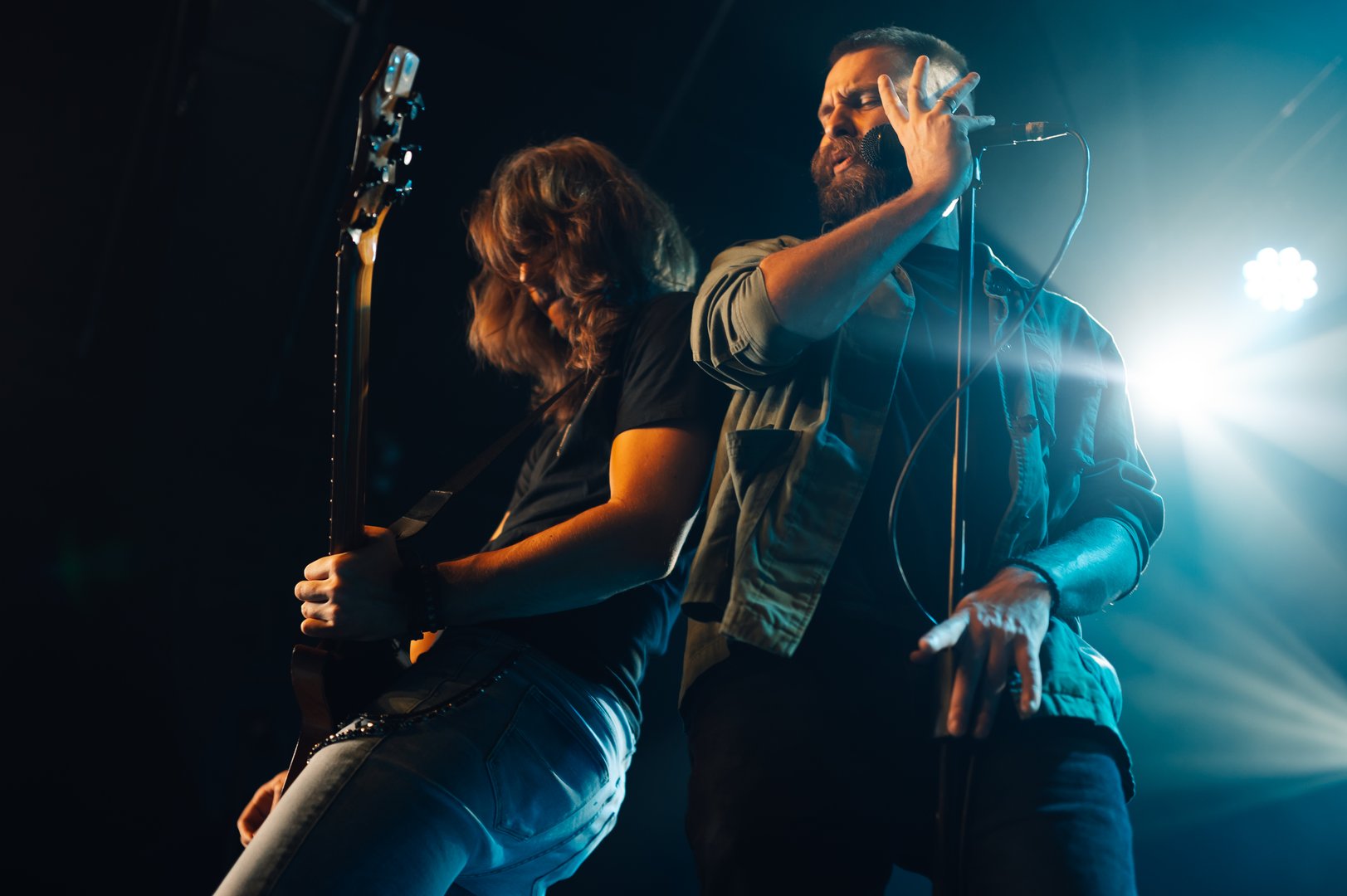 Two musicians playing with energy on a stage under blue lights