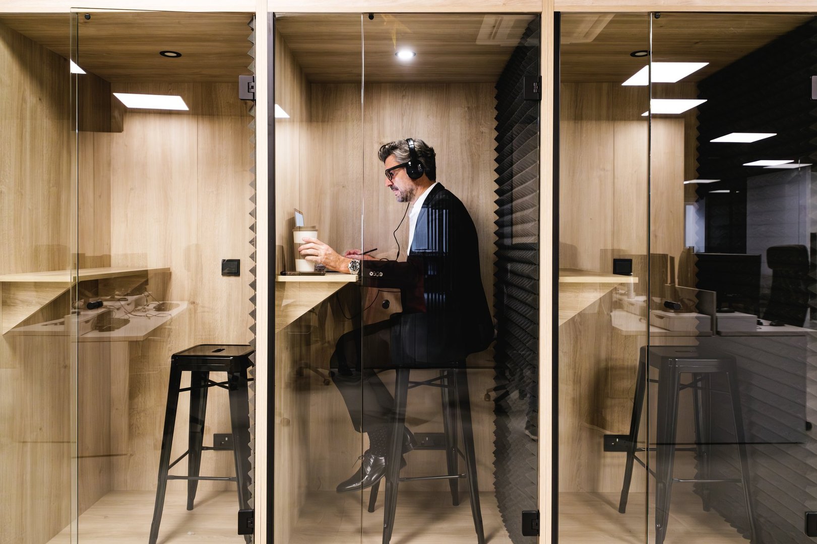 An executive engrossed in work uses headphones in a soundproof booth, ensuring privacy and concentration in a modern office