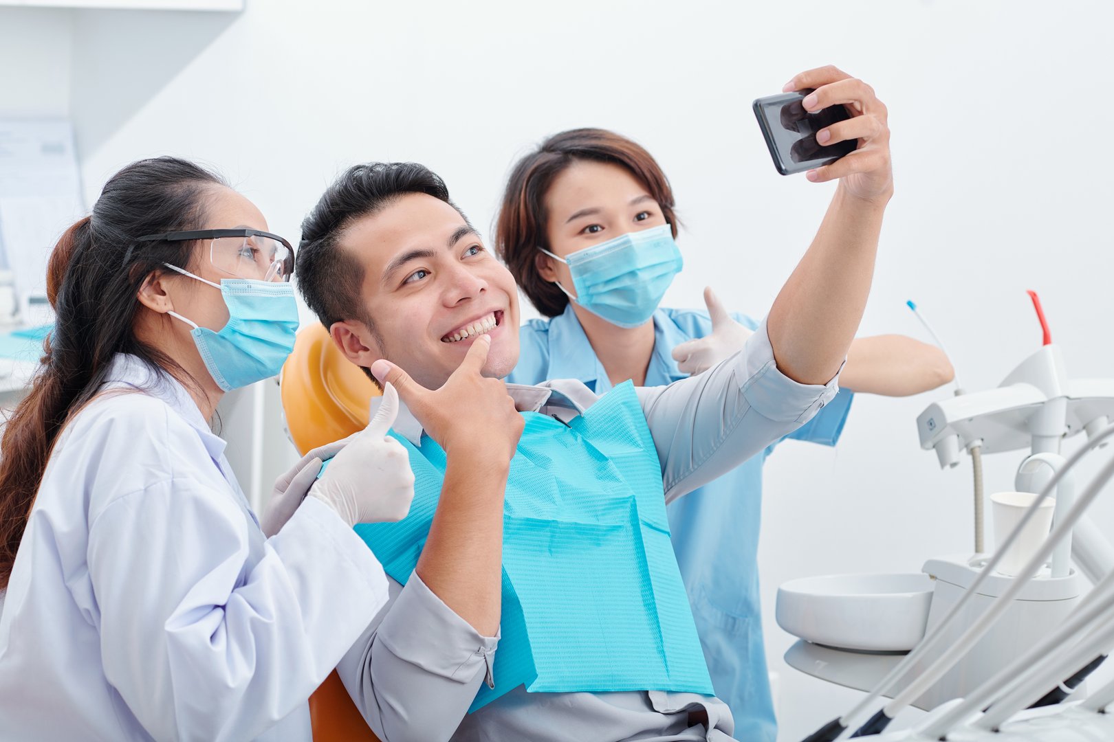 Young Asian man happy with his new smile taking selfie with dentist and her assistant for social media