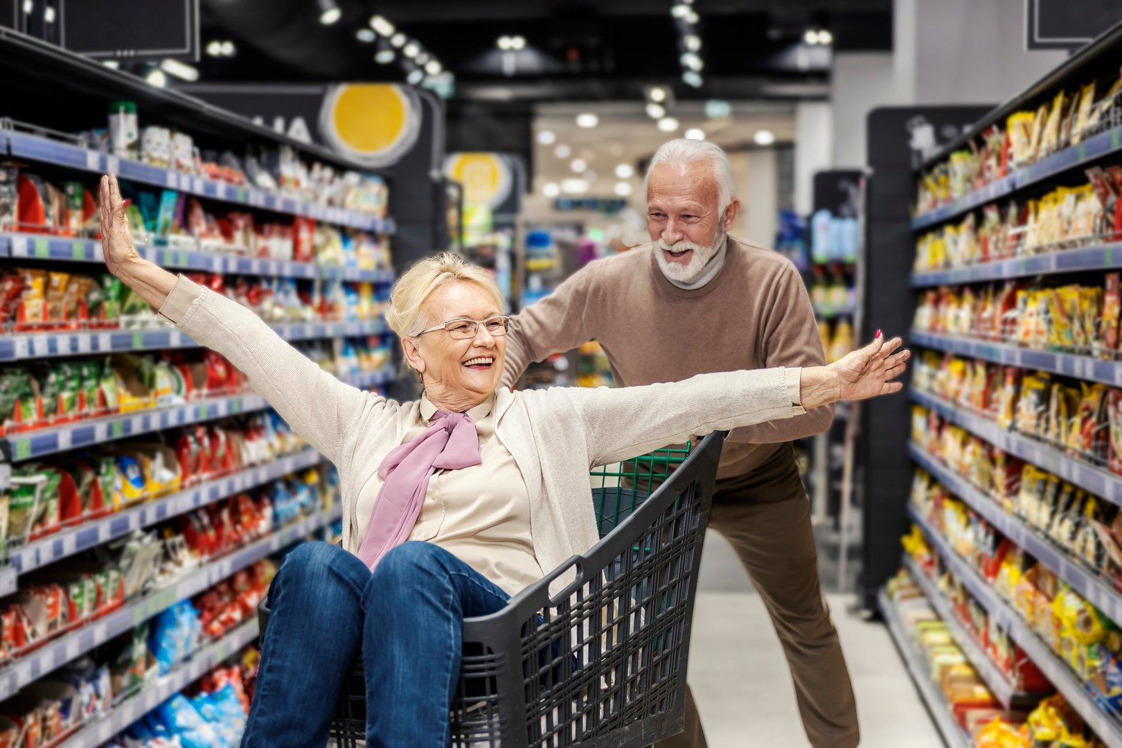 A playful grandparents driving in shopping cart at the supermarket.