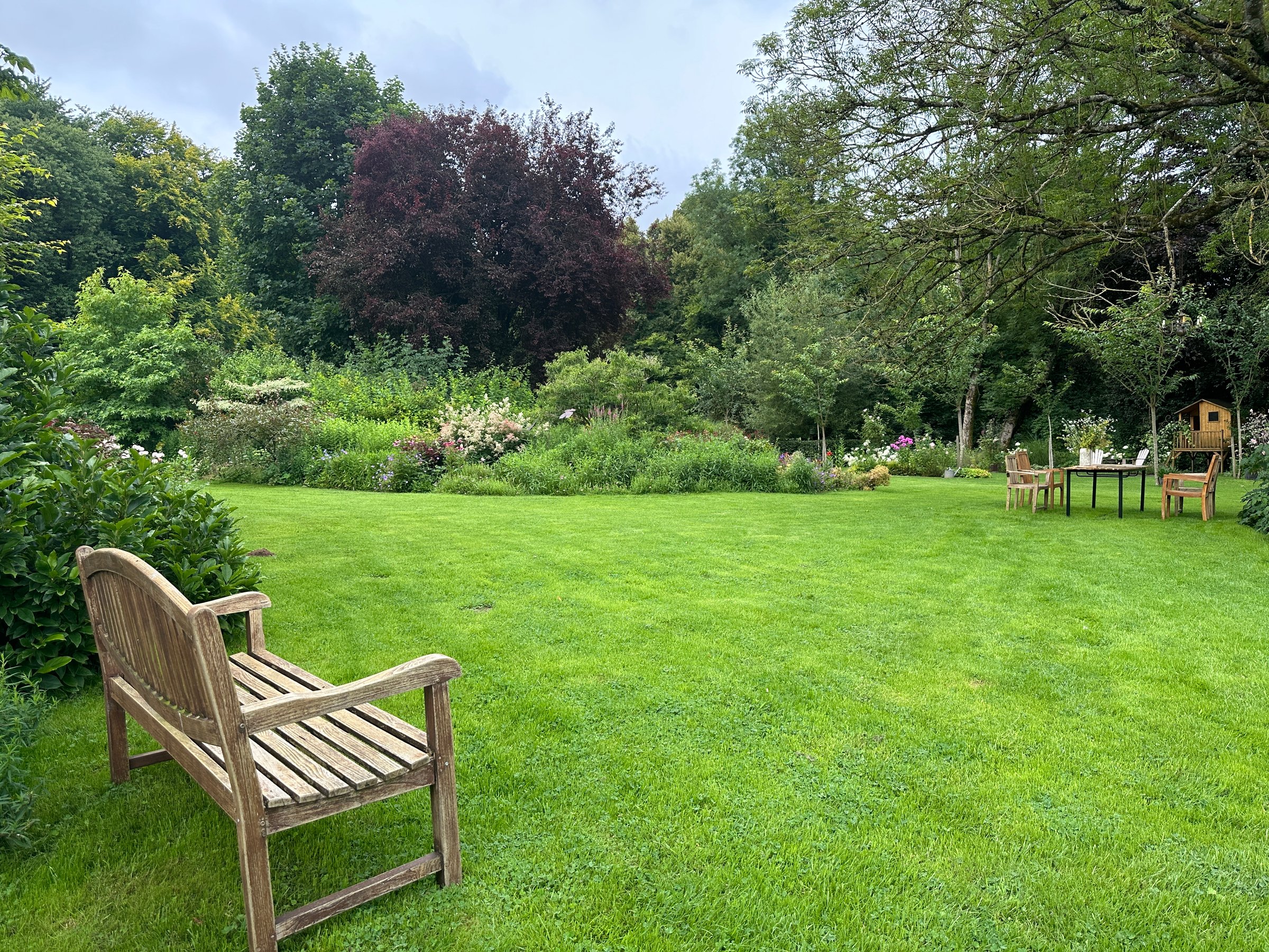 A green lawn stretches across the space, surrounded by lush plants and flowers, creating a peaceful retreat