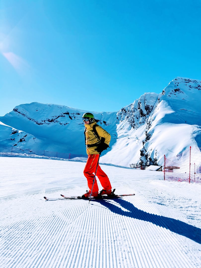 A skier in striking red pants surveys the snow-covered slopes, ready to glide down the freshly groomed trails under a clear blue sky.