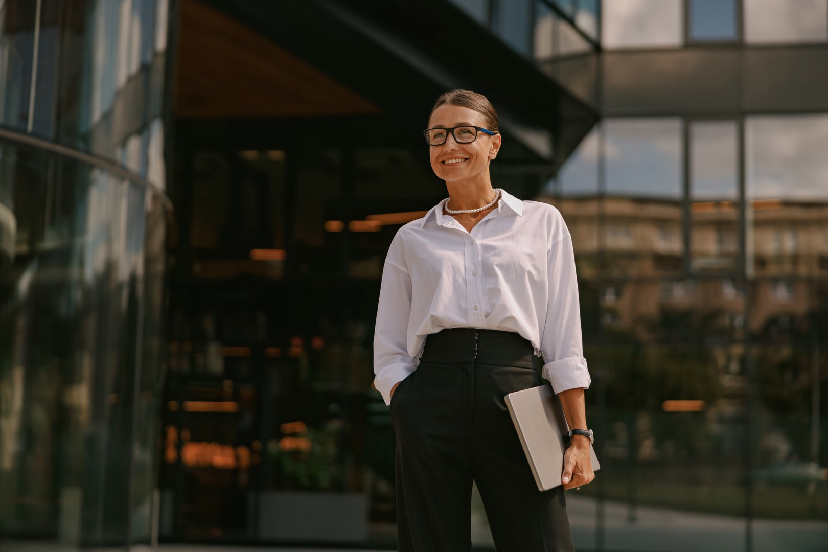 A professional woman in glasses poses confidently in a business setting, showcasing modern corporate style.