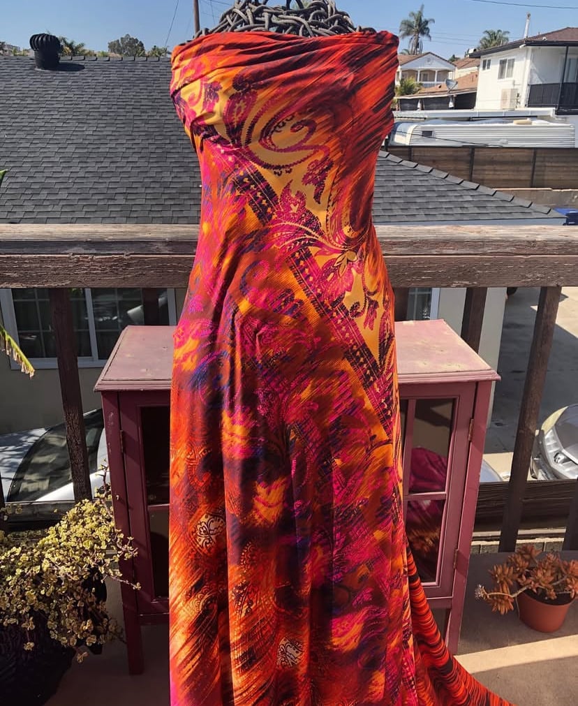Vibrant strapless dress on a mannequin with a colorful abstract pattern in reds, oranges, and yellows on a balcony.