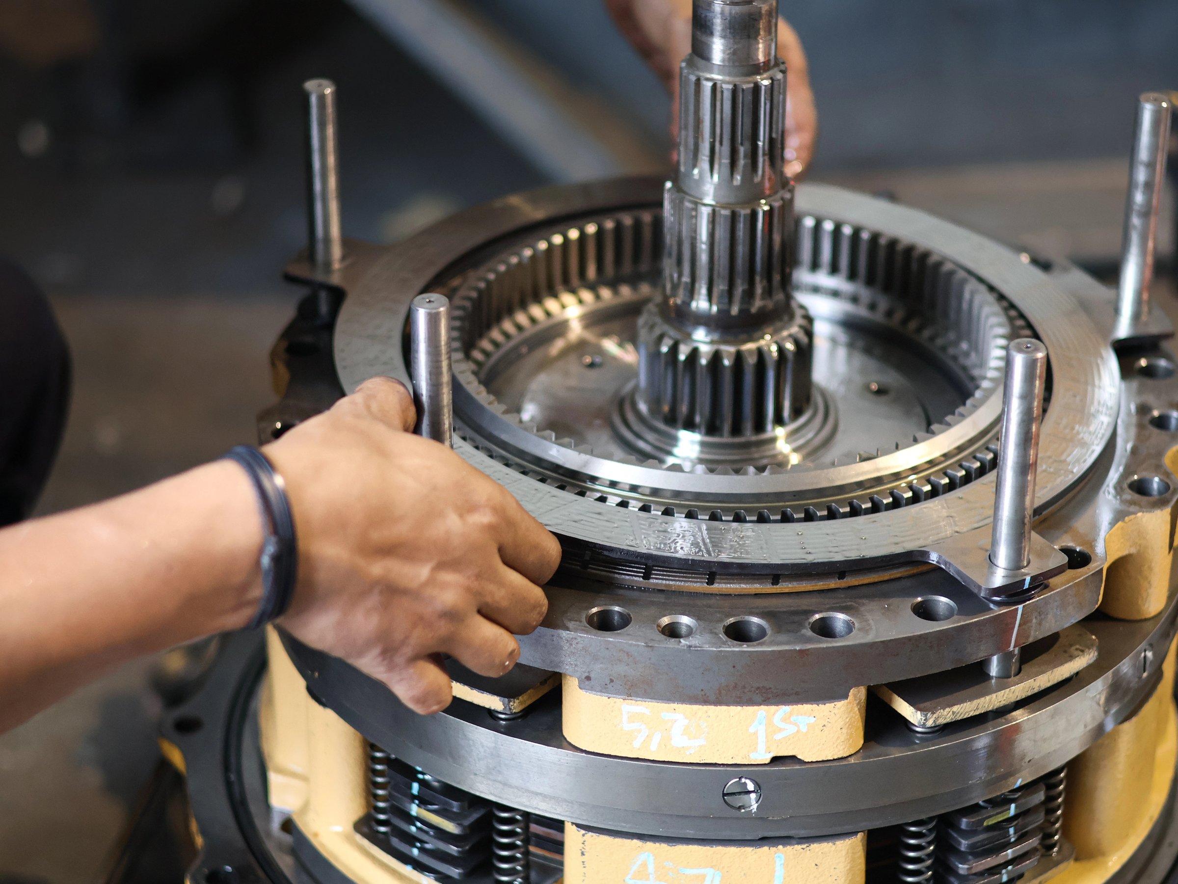 Worker hands with gloves assembling industrial clutch gear mechanism in workshop with precision tools.