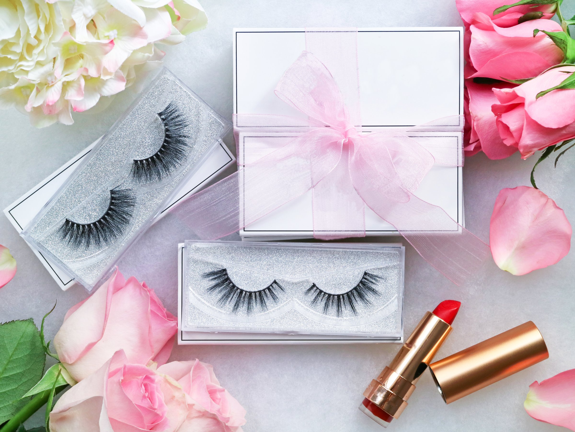 Top view of false eyelashes with its boxes as a gift with pink ribbon wrapped. And pink roses flower with it petals as well as a lipstick in a frame. Beauty make up and fashioned concept