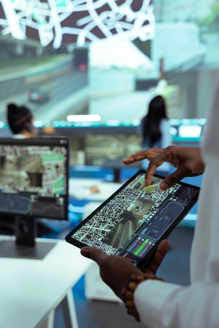 African american team leader monitoring courier activity around the city, looking for routes to avoid traffic and ensure fast delivery. Manager operates on tablet with CCTV footage and gps. Close up.