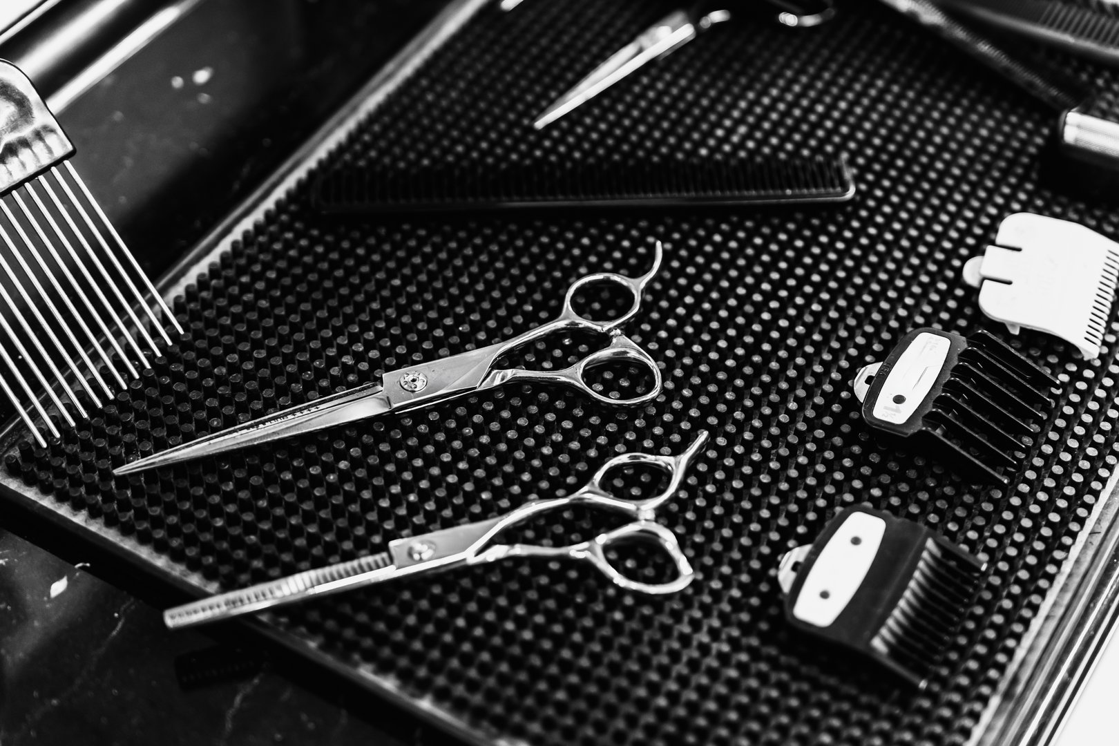Scissors, combs, and hair clipper attachments are neatly placed on a dark surface in a salon.