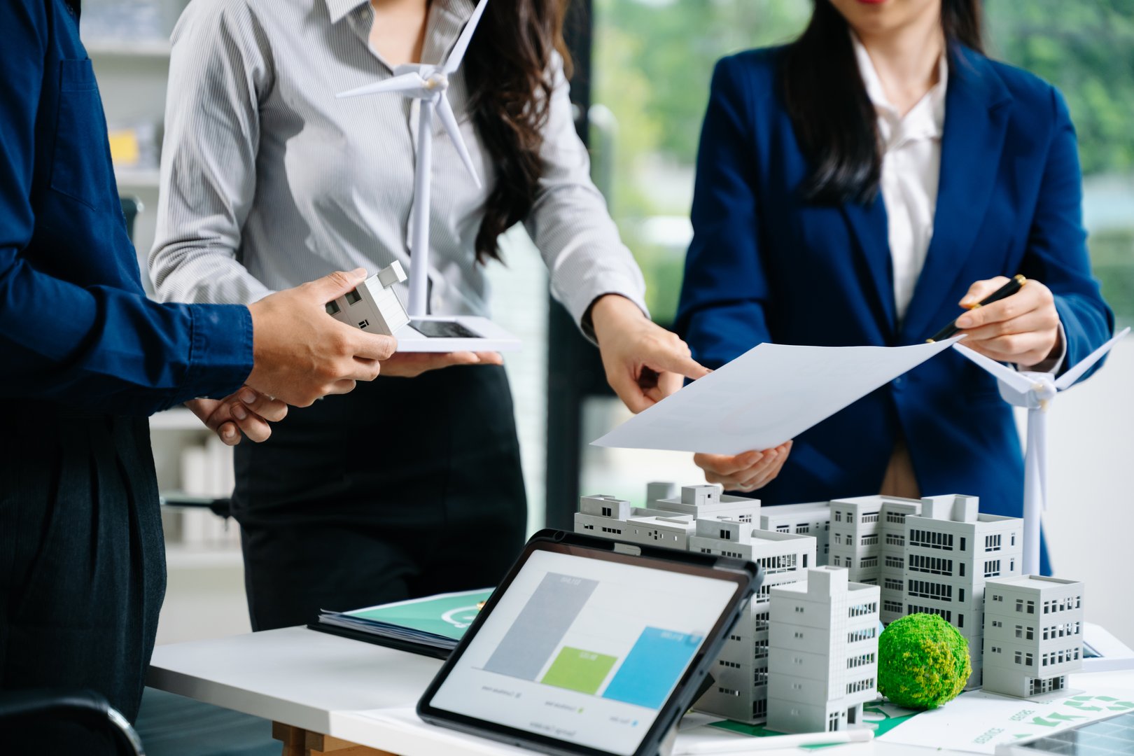 Professionals presenting wind turbine and building models during a meeting. Ideal for green energy, smart city planning, and sustainable business themes.
