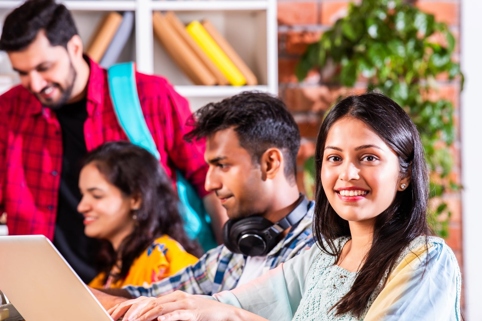 Indian asian college students in group using laptop computer pointing at blank or presenting or celebrating success, presenting blank placard, thumbs up success gesture, sitting on floor