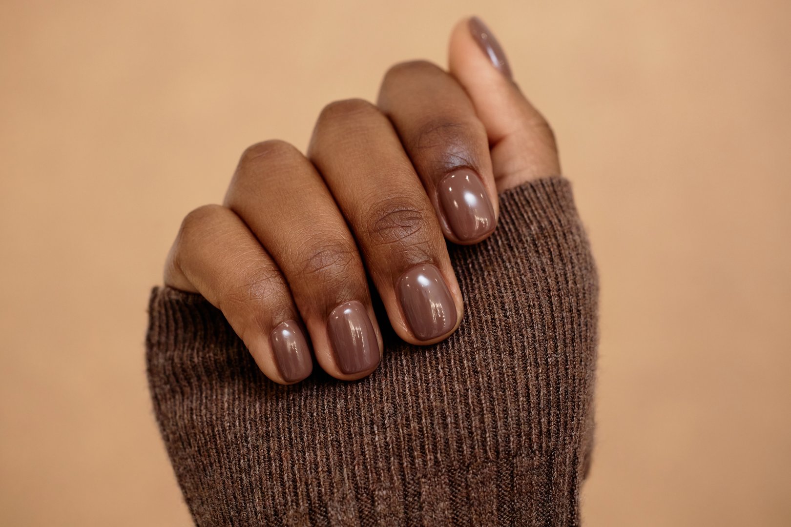 Close up shot of simple nail design in rich brown shade for autumn complementing outfit on beige background