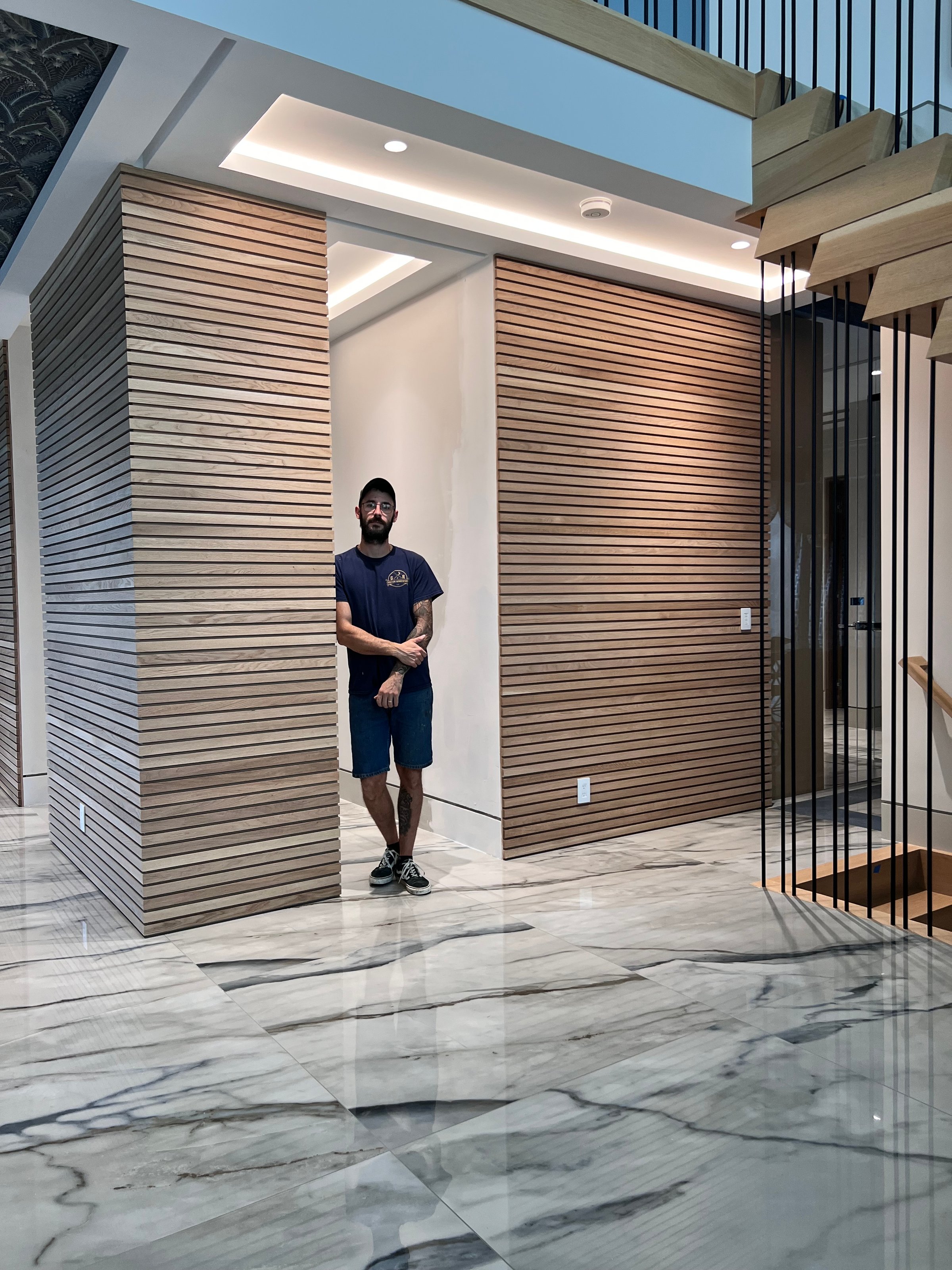 Man in casual outfit standing between wooden slat walls on a shiny marble floor in a modern interior setting.