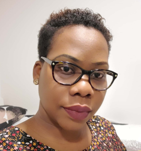 Person wearing glasses and a patterned top, posing for a selfie against a neutral background.