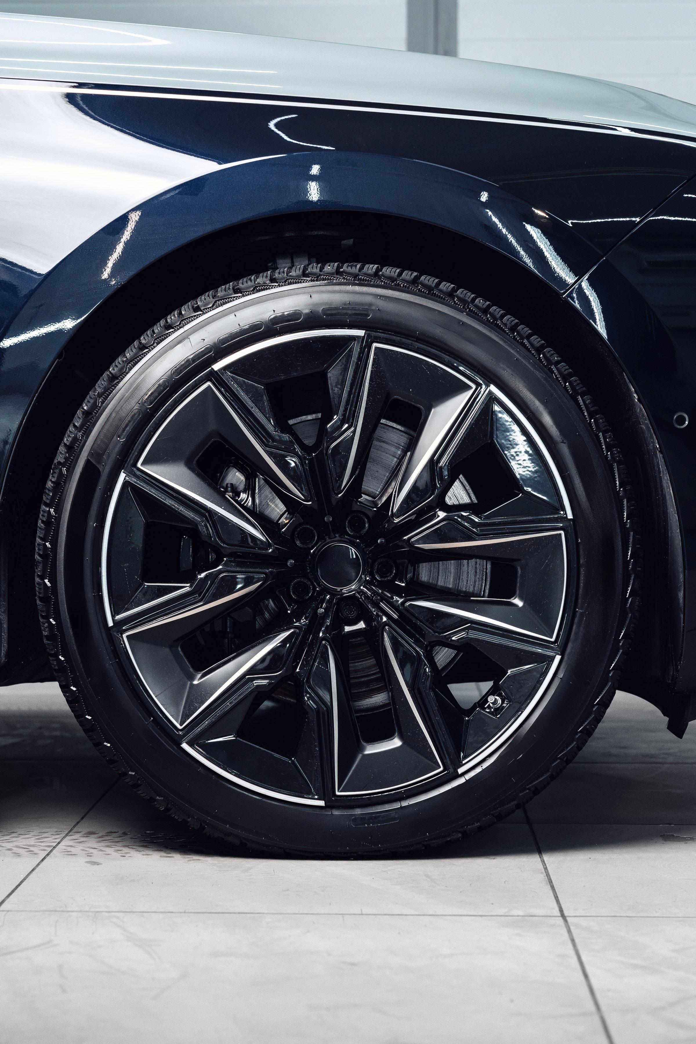 A close-up view highlights the intricate design of a black car wheel featuring bold spokes. This modern automotive detail captures the craftsmanship and style in a bright showroom.