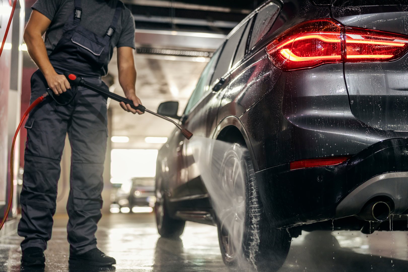Cropped picture of an unrecognizable car wash worker using a water gun for washing a car tyre.
