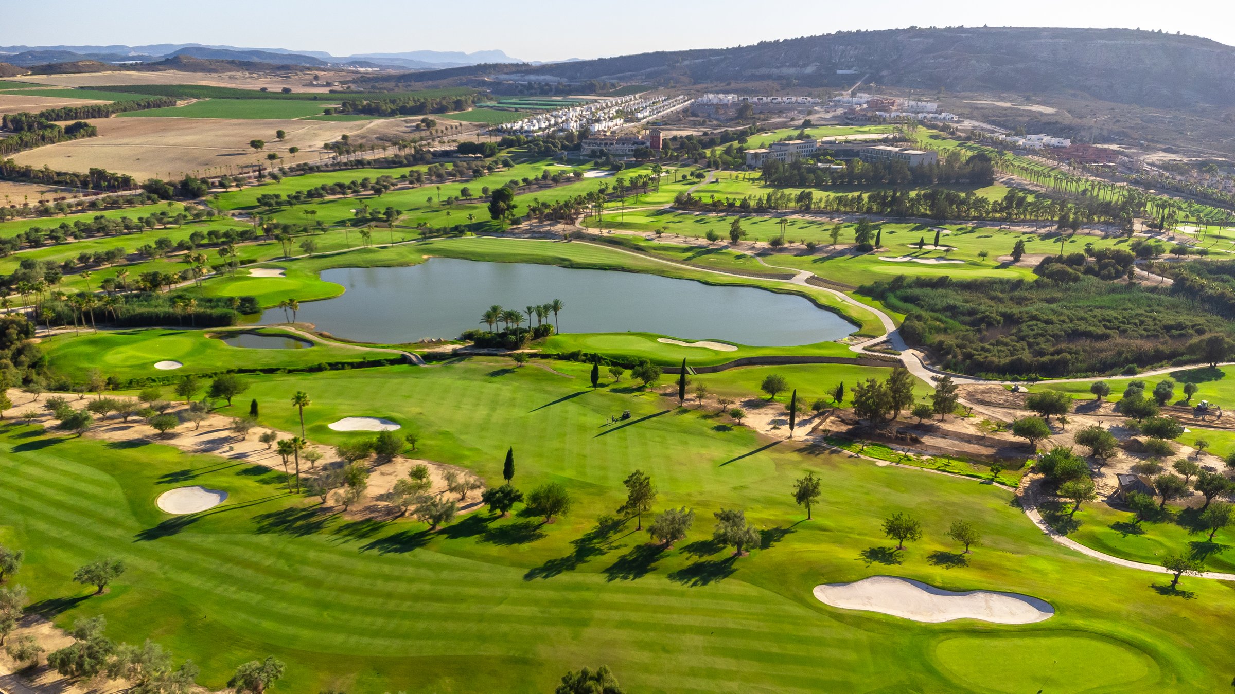 Wide aerial view of a luxury golf course with green grass and a lake