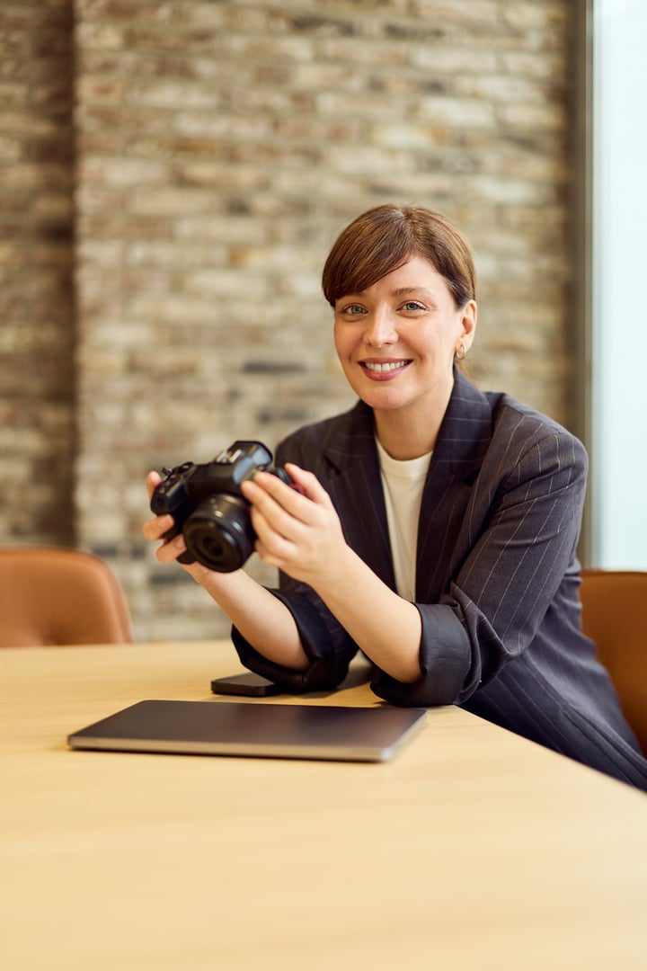 Professional woman with a camera in a bright, modern office setting, ready to shoot.