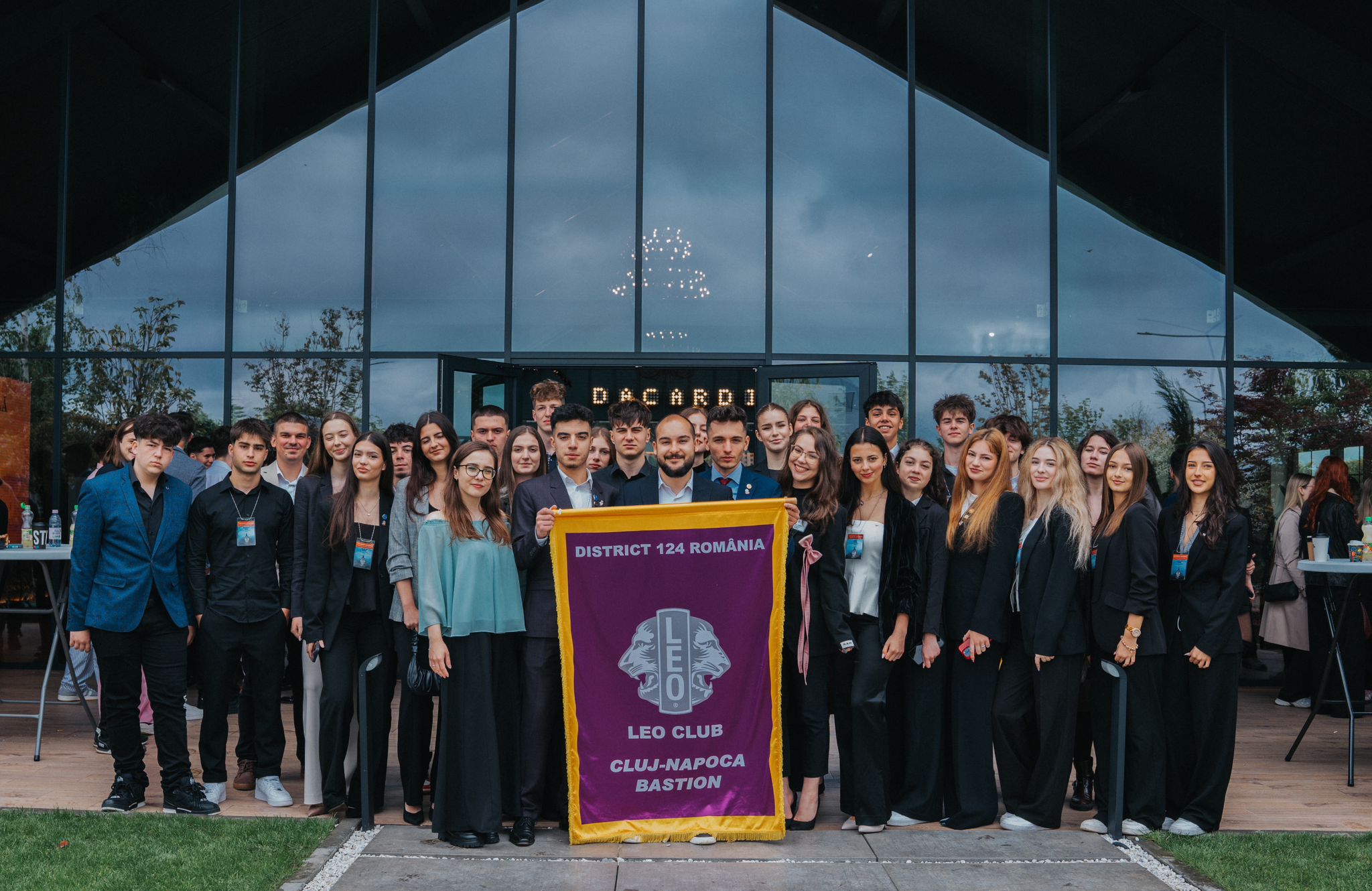 Group of young people in front of a building, holding a banner for Leo Club Cluj-Napoca Bastion, District 142 Romania.
