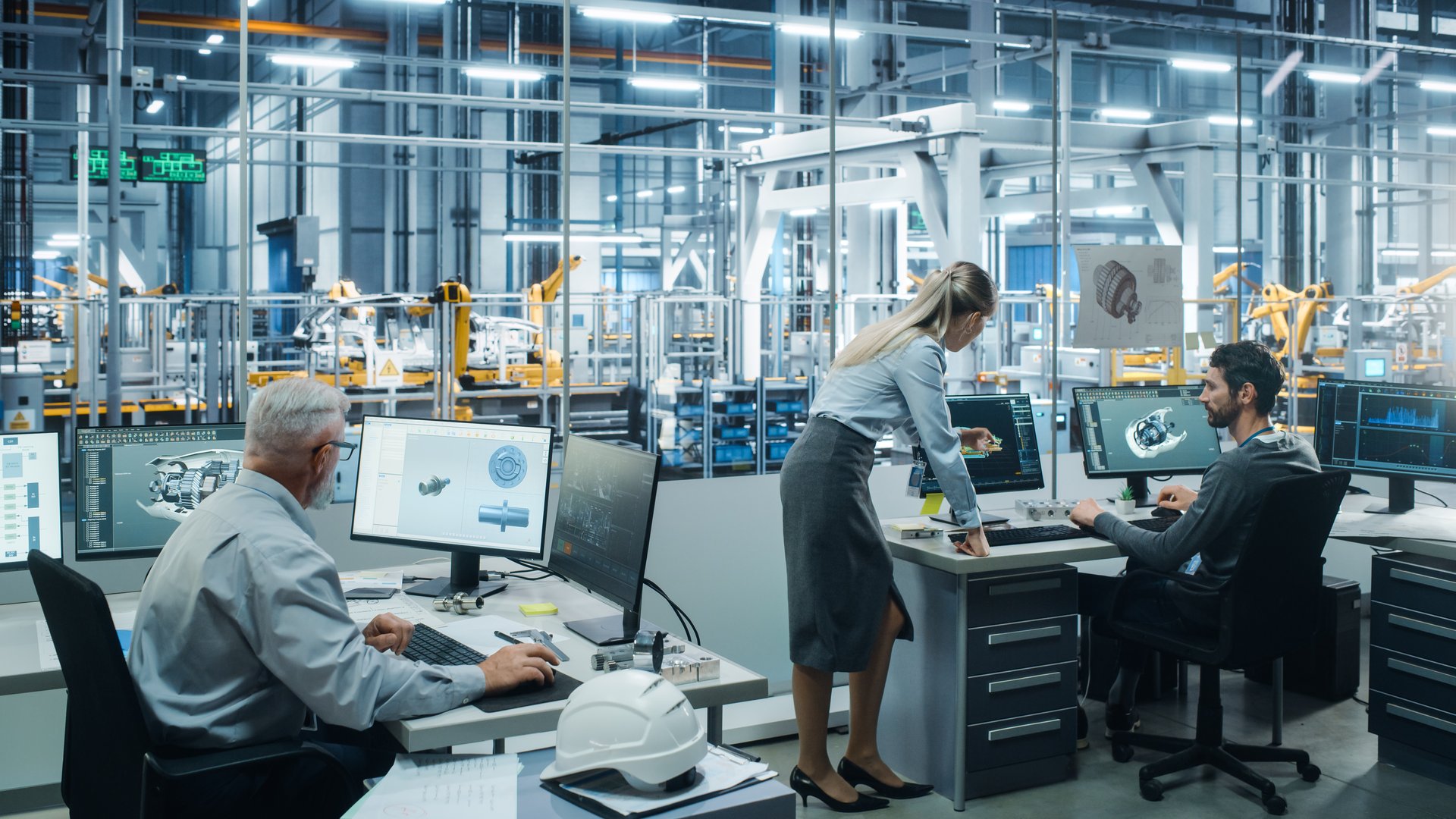Car Factory Office: Project Manager Talks to Engineer Working on Computer. CAD Software, 3D Turbine Engine, Electric Car. Automated Robot Arm Assembly Line Manufacturing Vehicles. Wide Shot