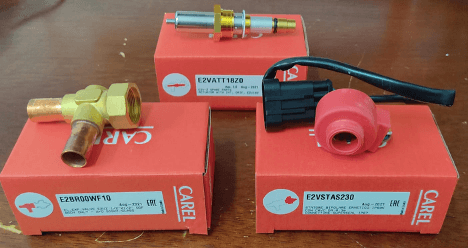 Carel HVAC components on red packaging boxes, including a valve, sensor, and electrical connector.