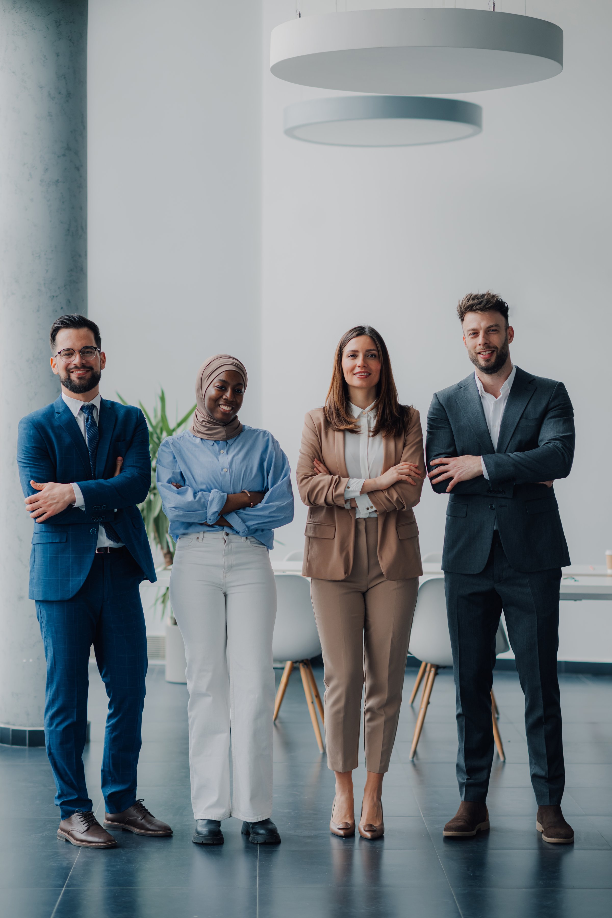Four businesspeople standing in their modern office with their arms crossed, smiling at the camera