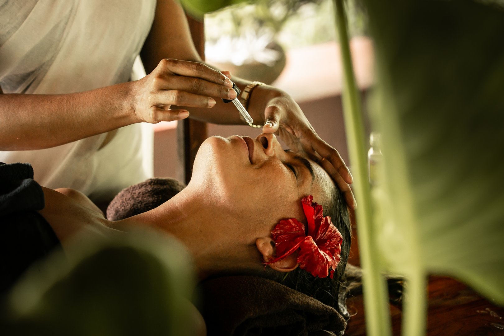 The staff of an Ayurveda clinic administers oil into the nose of a client lying on a wooden bed during a Nasya treatment. Nasya is an important Ayurvedic therapy used to cleanse and rejuvenate the nasal passages, sinuses, and respiratory system. Warm herbal oils, often infused with medicinal herbs, are gently dropped into the nostrils to help clear blockages, reduce inflammation, and promote better airflow. This treatment is believed to enhance mental clarity, reduce headaches, and alleviate symptoms of sinus congestion and respiratory issues. The use of a wooden bed is traditional, helping to ground the body while facilitating the deep therapeutic benefits of Nasya.