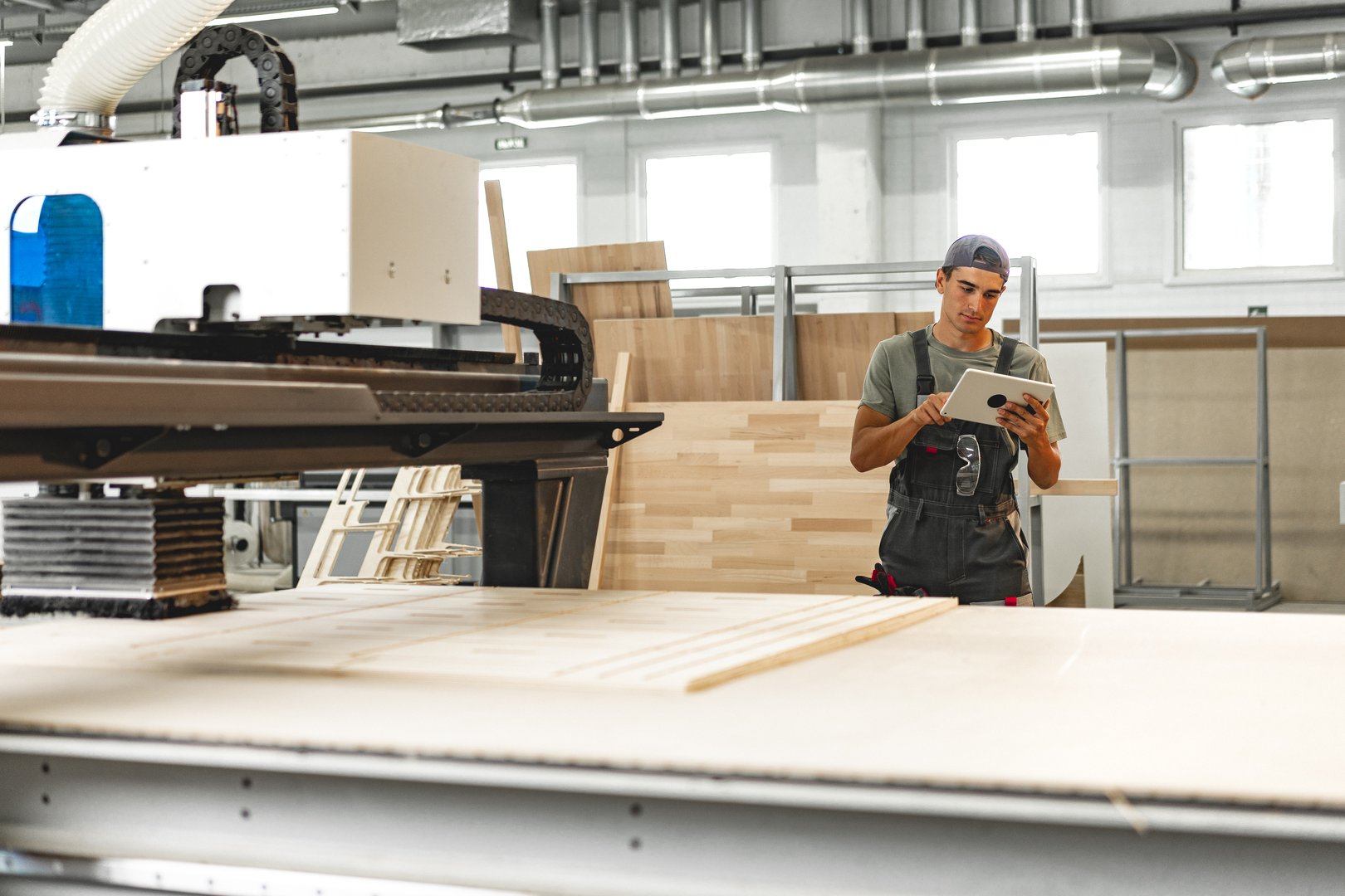 Young carpenter operating machine for wood processing at a furniture factory close up