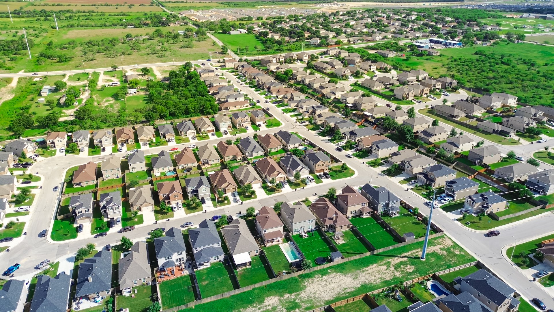 Suburban sprawl with vacant land for growth in suburbs San Antonio, Texas, row of two-story new development single family houses with large backyard, undeveloped land near a city, aerial view. USA