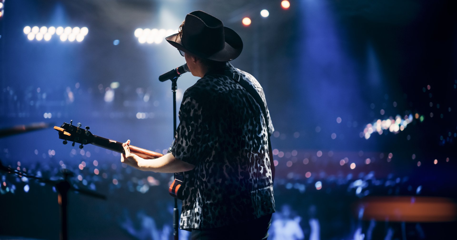 Portrait of a Handsome Young Man Singing a Country Song and Playing Guitar at a Music Festival. Cinematic Neon Spotlights Illuminates the Star, His Romantic Presence and Lyrics Electrify the Stage