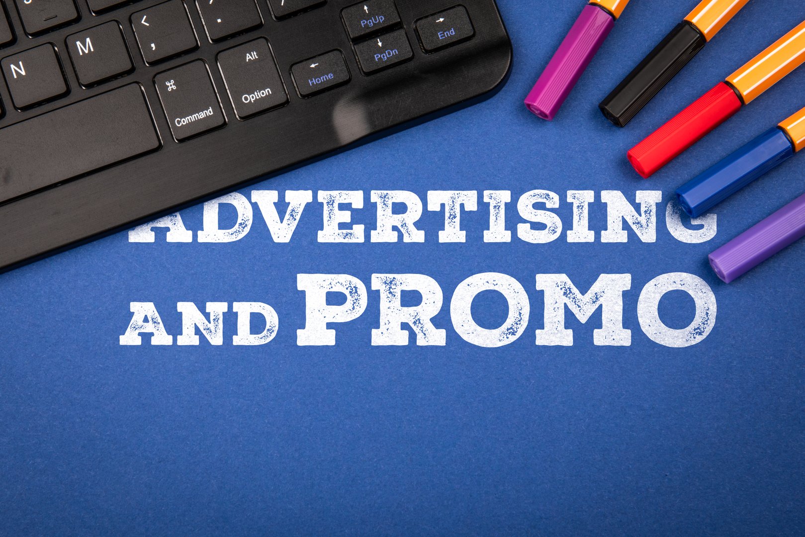Text Advertising and Promo on Blue Background with Keyboard and Colorful Markers Representing Marketing and Branding Concept.