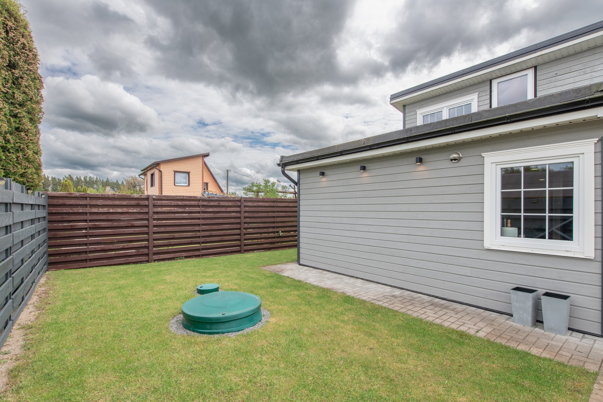 A serene backyard featuring a lush green lawn, wooden fences, and modern residential architectural elements under a partly cloudy sky.