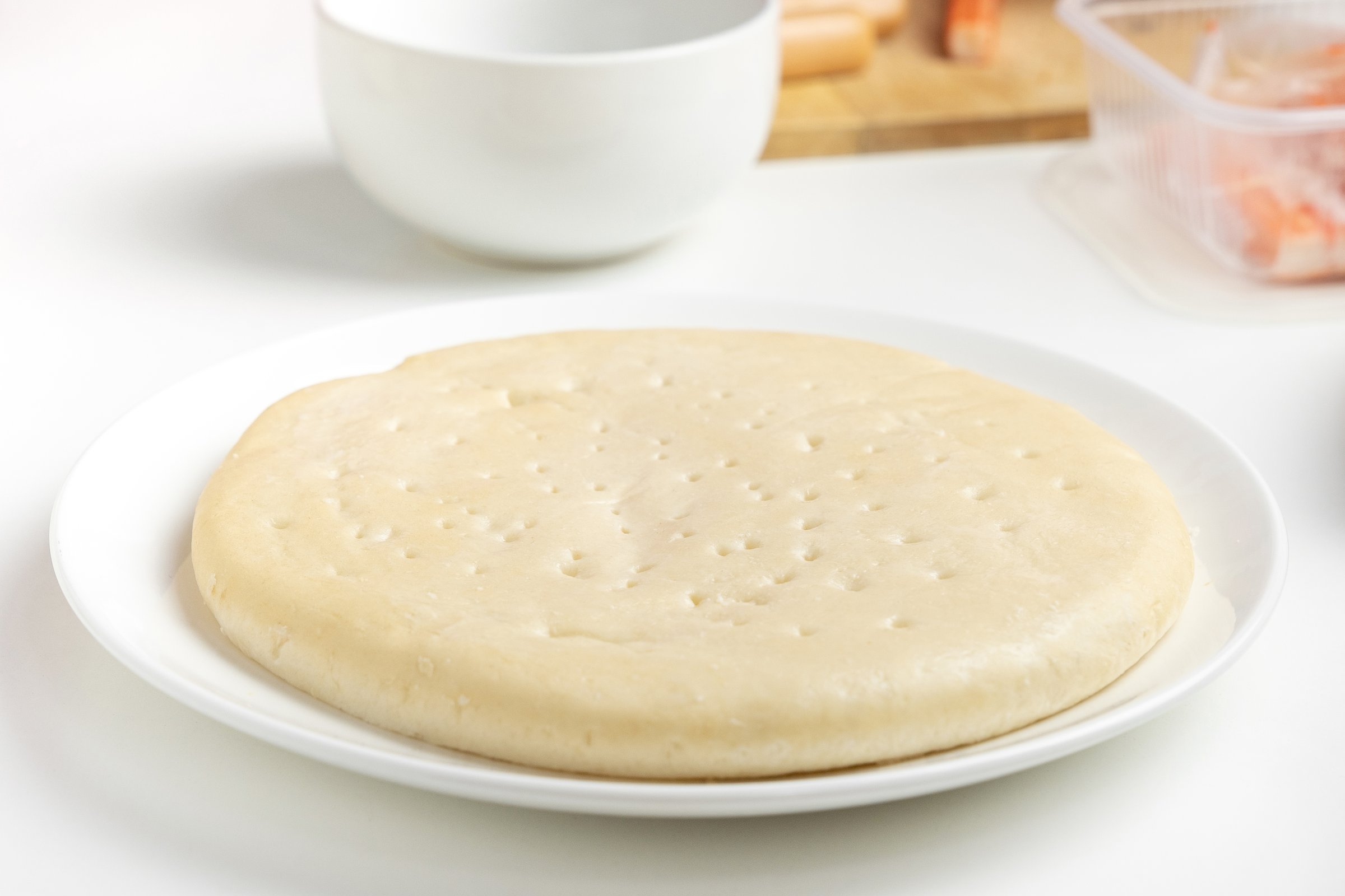 Pizza dough is placed in a white plate during preparation before being put into the oven.