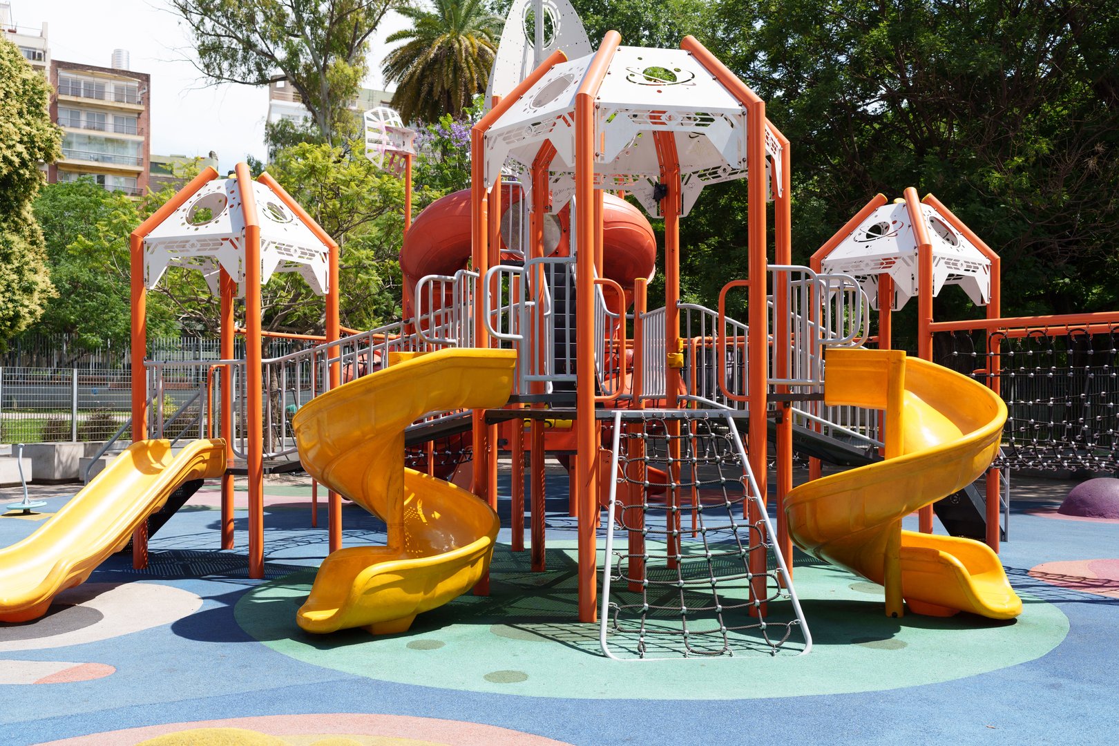 Colorful playground equipment featuring orange posts, yellow slides, and climbing nets on a rubberized surface, providing a fun and safe environment for children's outdoor play and recreation