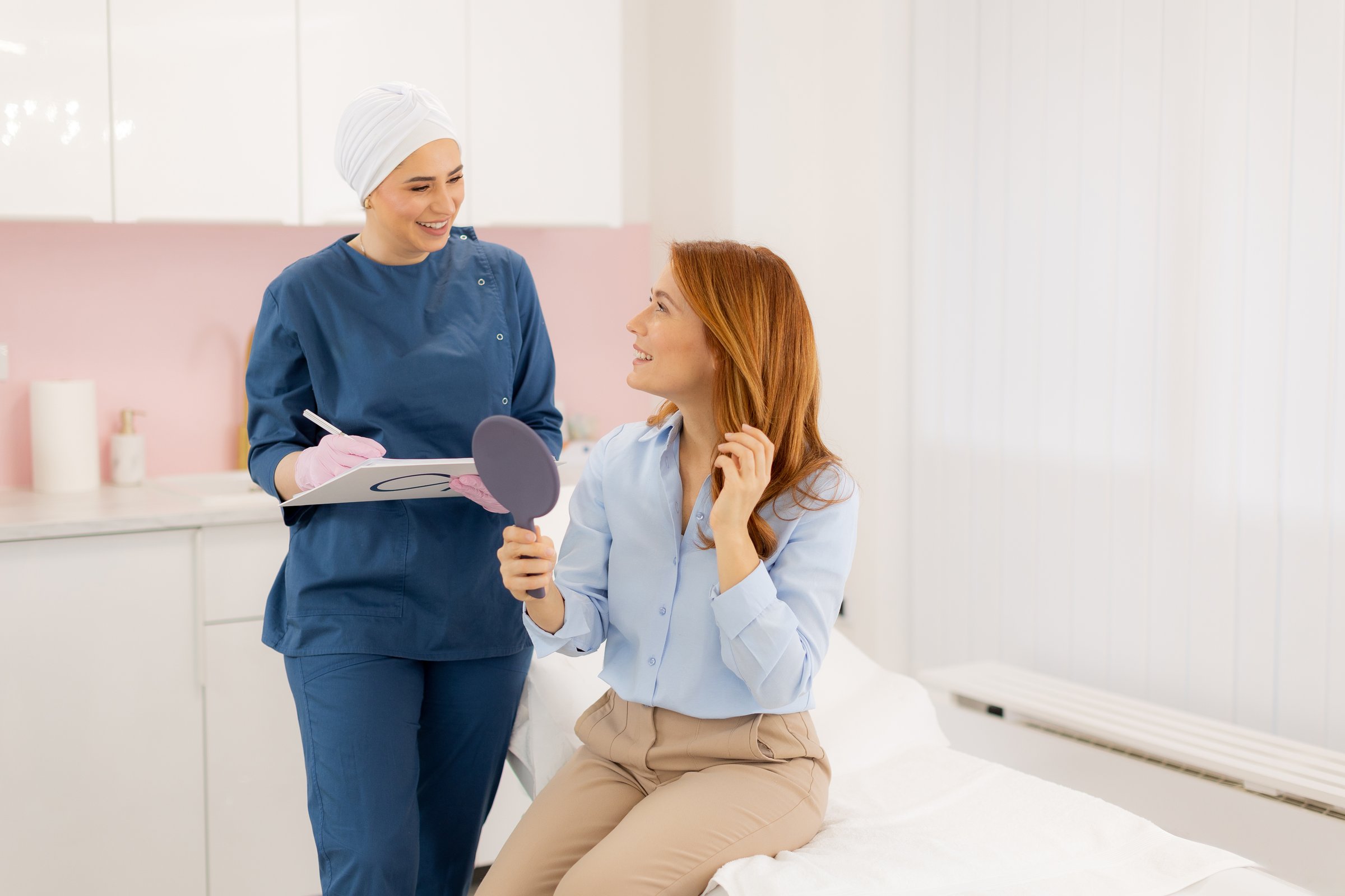 In a bright beauty clinic, a skilled specialist consults with a client sitting comfortably on an examination table, discussing skincare options while holding a mirror.