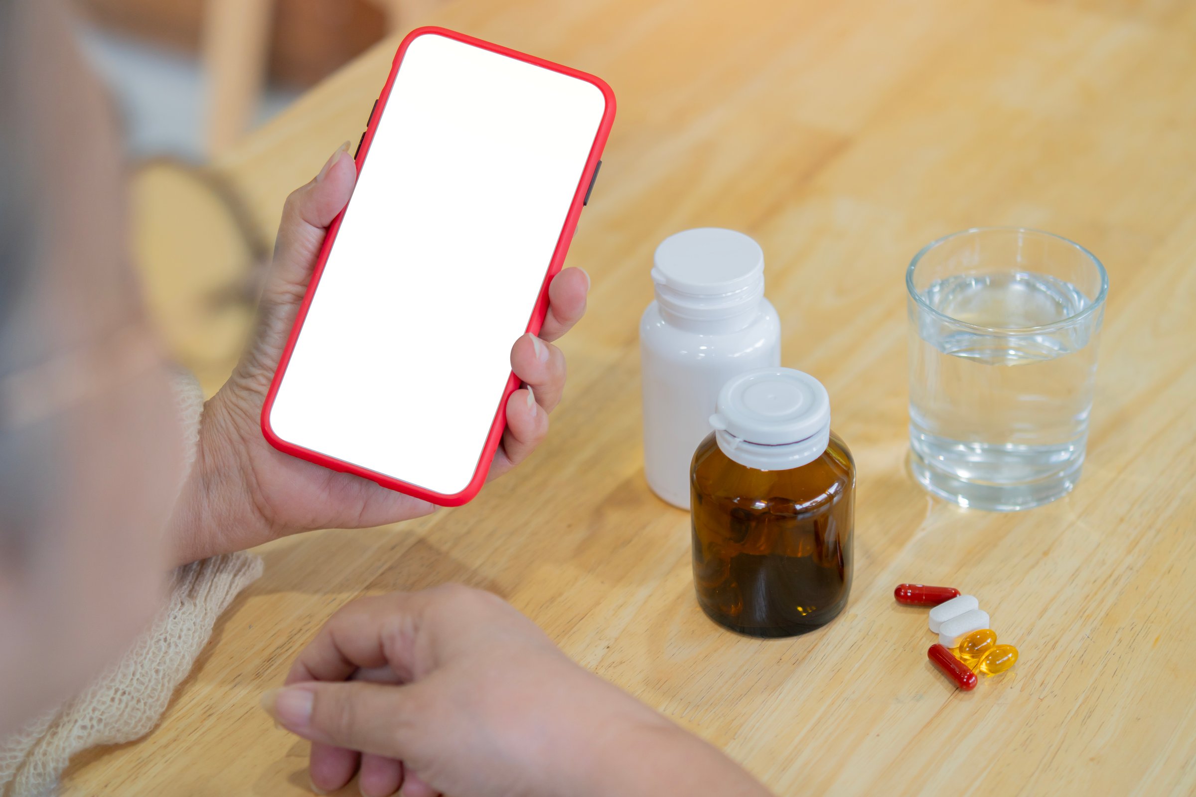 Mature woman with phone isolate screen and medicine bottle with glass of water on the wooden table. Copy space.