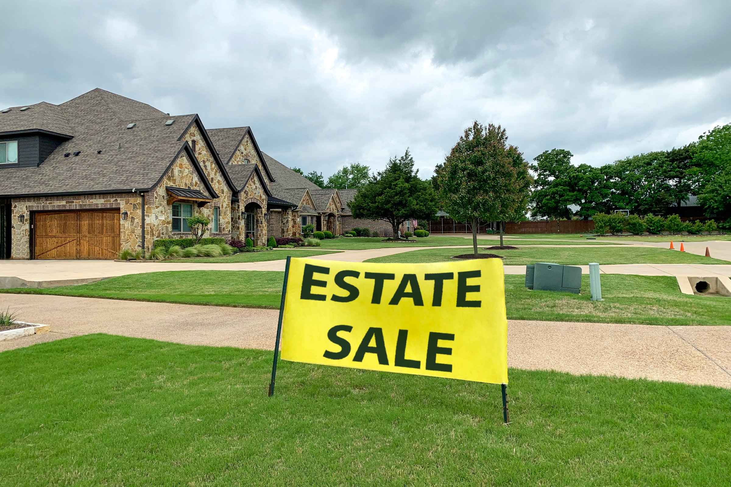 Outdoor shot of residential house with road and neat lawn in front of it, big yellow sign with estate sale inscription. Sale of mansions.