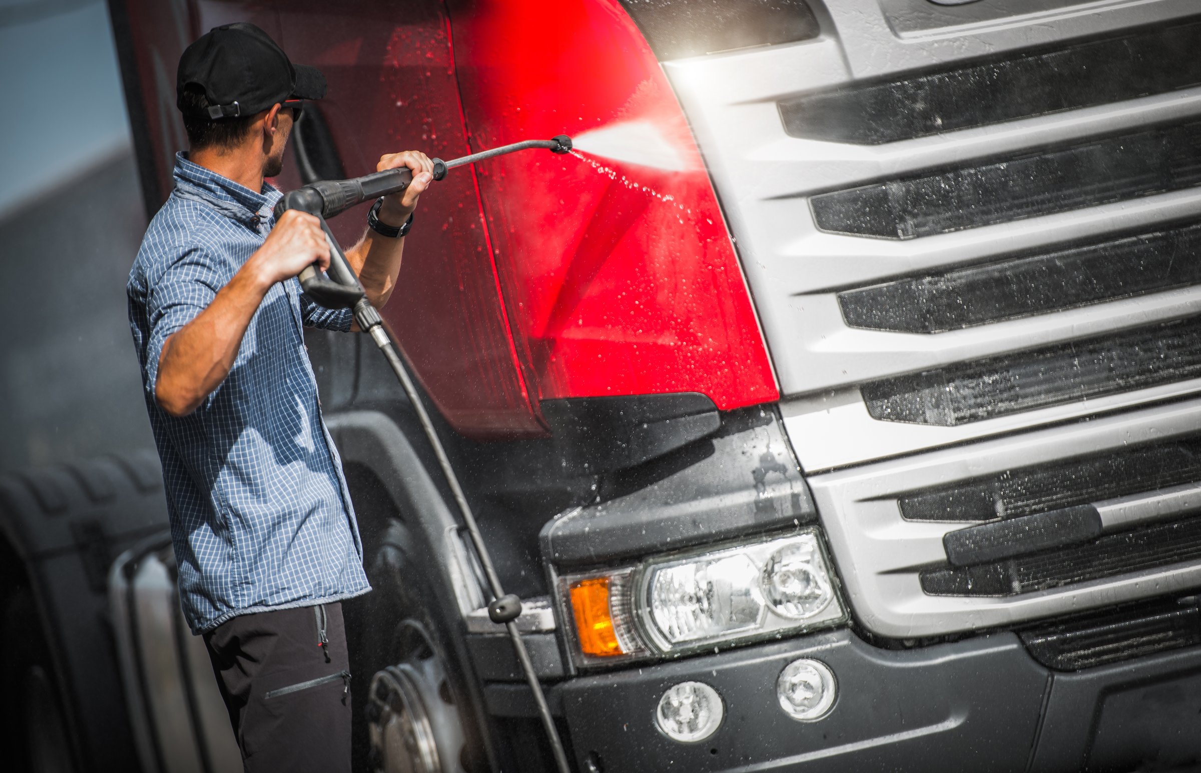 Truck Driver Washing His Semi Truck Tractor. Sunny Day in the Transportation Base.