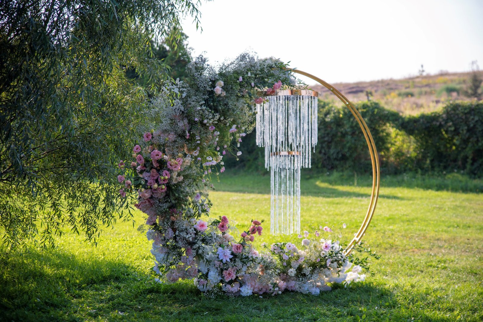 Round wedding arch with pink flowers and hanging crystal in summer