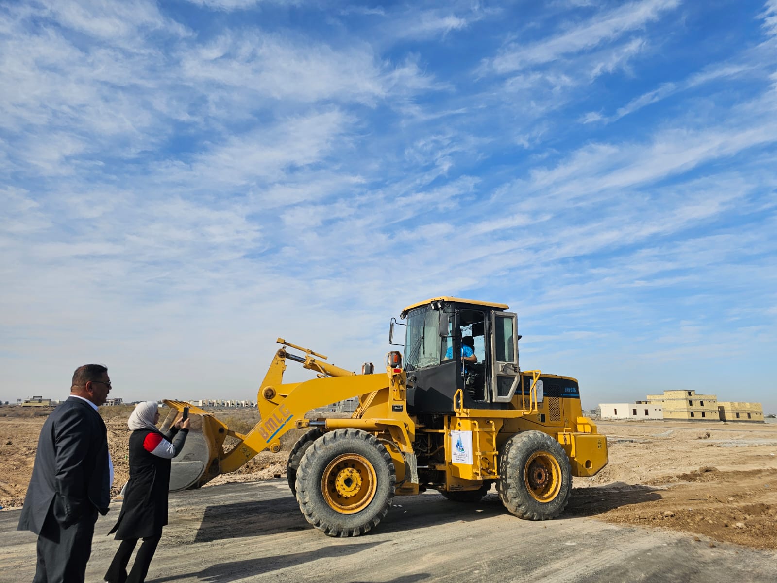 Yellow bulldozer on construction site with two people observing, clear blue sky in the background.