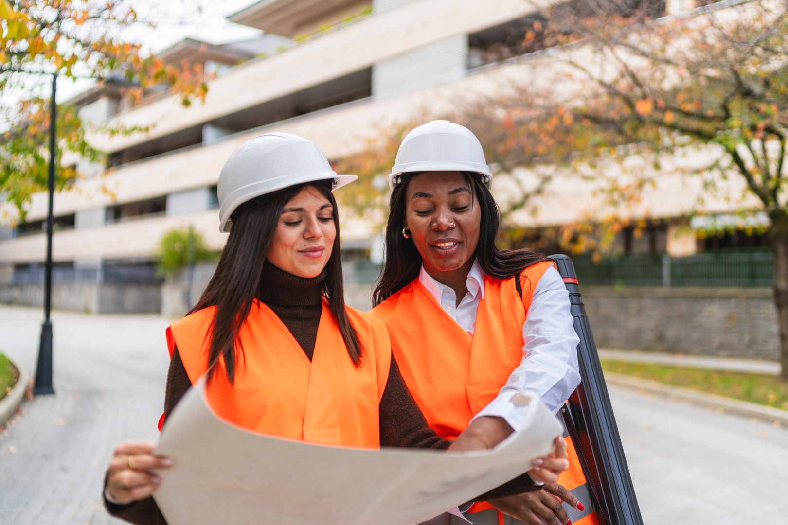 Two diverse female engineers reviewing construction blueprint discussing project details